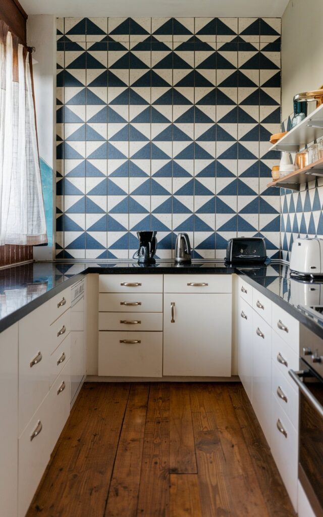 A photo of a fully furnished modern Bauhaus kitchen with bold geometric wall tiles in a striking pattern. The kitchen features a wooden floor, white cabinets, and a black countertop. There is a black kettle, a toaster, and a coffee maker on the countertop. The geometric wall tiles have a blue and white pattern. The room has a window with a curtain.