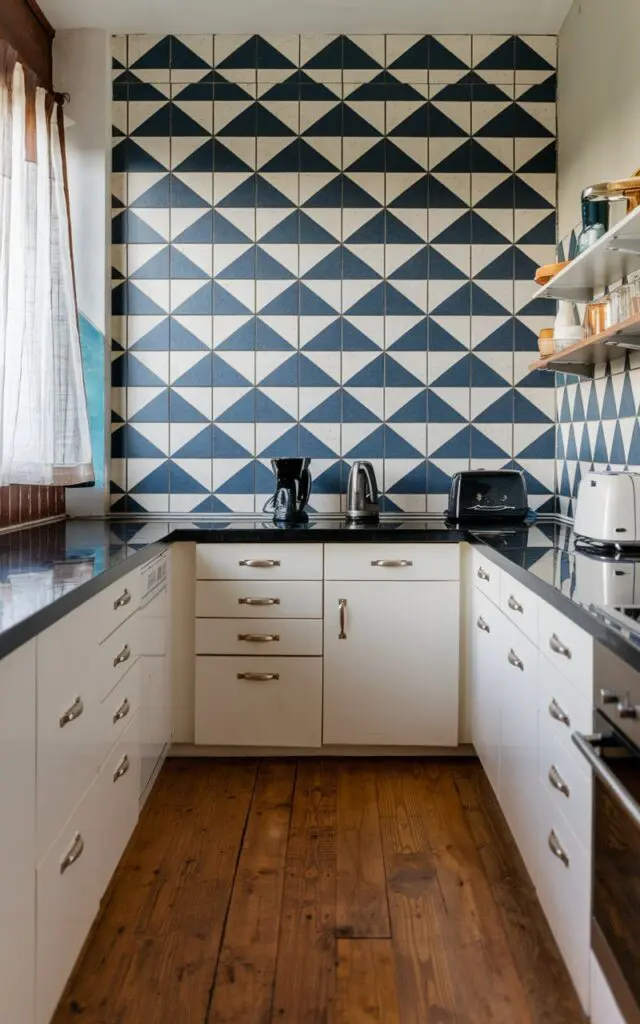 A photo of a fully furnished modern Bauhaus kitchen with bold geometric wall tiles in a striking pattern. The kitchen features a wooden floor, white cabinets, and a black countertop. There is a black kettle, a toaster, and a coffee maker on the countertop. The geometric wall tiles have a blue and white pattern. The room has a window with a curtain.