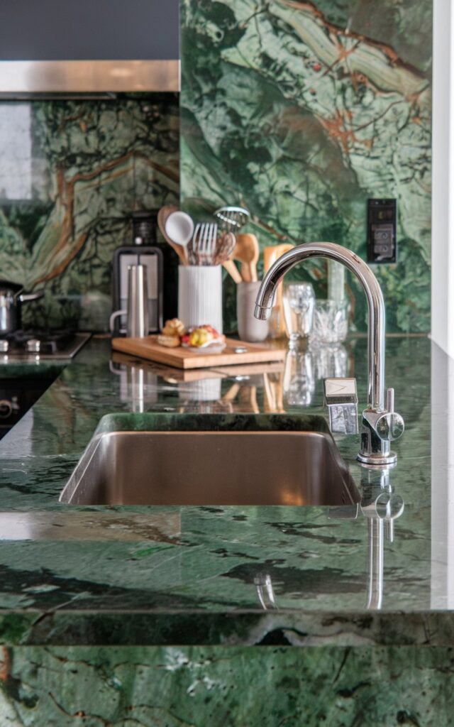 A modern luxurious kitchen having a green quartzite countertop with veining. The countertop has sink, utensils, and other essentials. Show closer view
