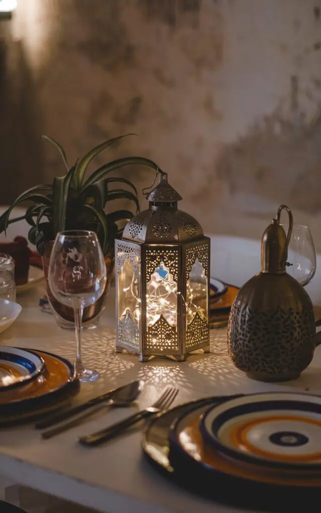 A photo of a boho-style kitchen dining table with a Moroccan design lantern at the center. The lantern has a fairy light inside it. The table has other functional elements, such as a plant, a decorative item, and a charger plate. The setup is perfect for date nights. The background has a rustic charm.