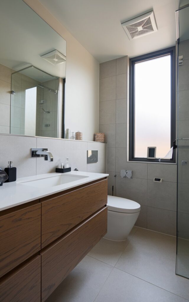 A photo of a modern half bathroom with a sleek vanity and a wall-mounted faucet. The bathroom is clutter-free and organized. The half bathroom is fully furnished with a toilet, a wall-mounted faucet, and a few bathroom accessories. The walls and floor are tiled. There is a window in the room.