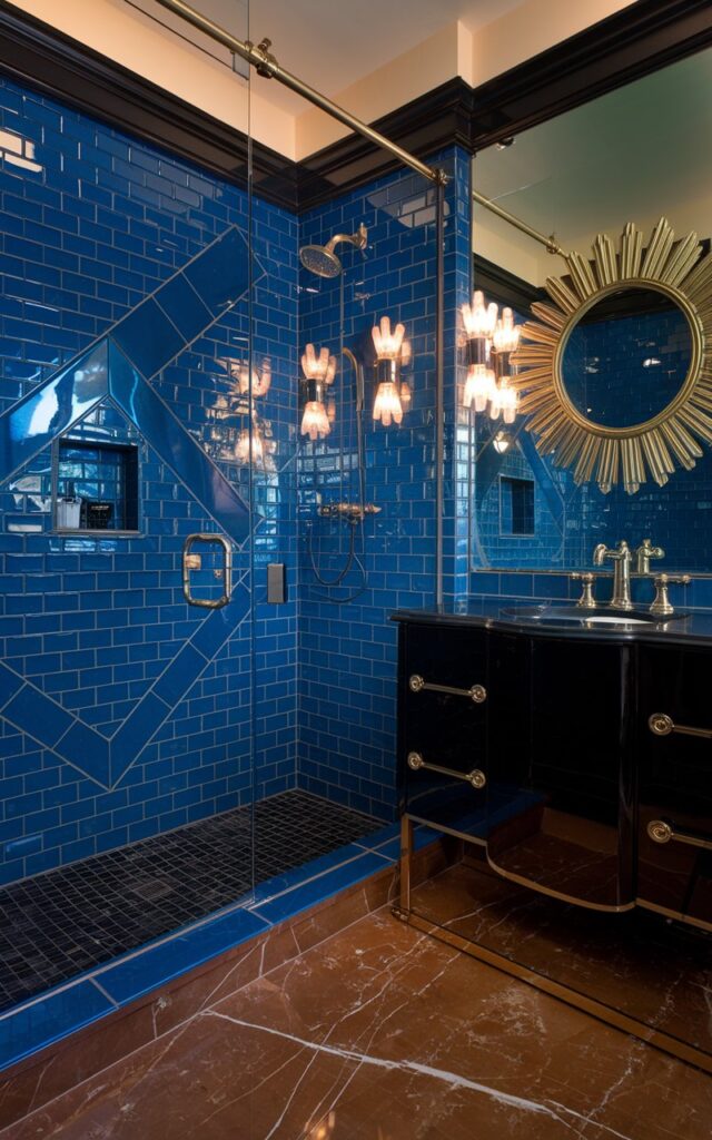 A photo of a sleek Art Deco bathroom with a cobalt blue subway tile shower. The shower has sharp geometric patterns and a glossy finish. The space features black and gold accents, including a streamlined black vanity with gold hardware and an ornate sunburst mirror. The floor is made of rich marble with contrasting dark grout. Vintage-style brass light fixtures provide warm, glamorous lighting. The overall vibe is luxurious, dramatic, and distinctly 1920s-inspired, with clean lines and bold color contrasts.