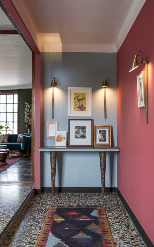 A photo of a mid-century eclectic hallway leading to a living room. The hallway has a bold painted accent wall and terrazzo flooring. There is a patterned runner on the floor. Above a narrow console with tapered legs, there are 2-3 small framed artworks. Each artwork is individually lit by a slim brass picture light. The overall space is brimming with personality and curated charm.
