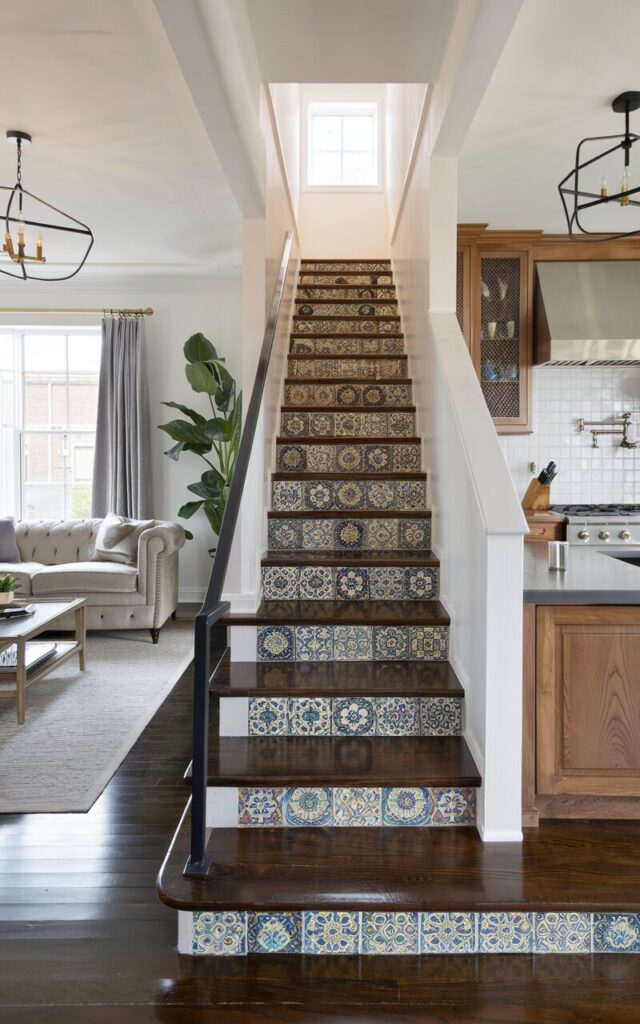A photo of a modern-traditional home interior with a fully furnished living room and kitchen. The living room has a plush sofa, a coffee table, and a potted plant. The kitchen has wooden cabinetry, a stove, and a sink. The sleek stairs are positioned between the living room and kitchen, with vibrant Moroccan patterned tiles on the risers. The stair treads are polished dark wood, and there's a simple black metal railing. The lighting fixtures in both spaces are elegant.