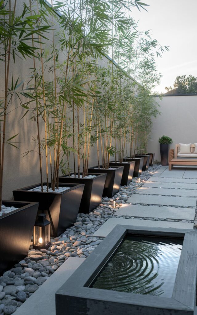 A photo of a Zen chic backyard with a modern feel. Along one side, tall potted bamboo plants are arranged in sleek, matte black ceramic containers, forming a natural green screen that hides an unsightly view. The bamboo sways gently, adding a soothing sense of movement and privacy. Nearby, a low teak bench with cream cushions invites quiet reflection, positioned beside a rectangular stone water feature with soft ripples. The ground is layered with smooth river pebbles and stepping stones leading toward a minimalist patio space. Lantern-style lights and subtle ground spotlights accentuate the bamboo's height, blending elegance with serene outdoor living.